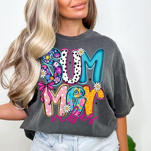 May include: Dark gray t-shirt with the words "SUMMER VIBES" in a colorful, floral, and polka dot design. The letters are outlined in black and feature daisies and a pink bow.
