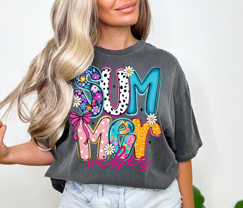 May include: Dark gray t-shirt with the words "SUMMER VIBES" in a colorful, floral, and polka dot design. The letters are outlined in black and feature daisies and a pink bow.