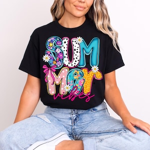 May include: Black t-shirt with the words "SUMMER VIBES" in a colorful, playful design. The letters are decorated with floral patterns, polka dots, and animal print, with daisy accents. A pink bow is also included.