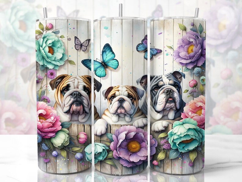 Op de afbeelding: Drie Engelse Bulldogs die uit een bloemstuk kijken. De bloemen zijn roze, paars en blauw met een houten achtergrond. De honden zijn wit met zwarte vlekken en hebben een lieve uitdrukking.