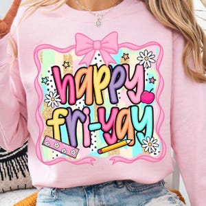 May include: Pink sweatshirt with a colorful graphic that says "Happy Fri-Yay." The design includes a pink bow, stars, daisies, an apple, a ruler, and a pencil. The background has gold glitter and pastel stripes.