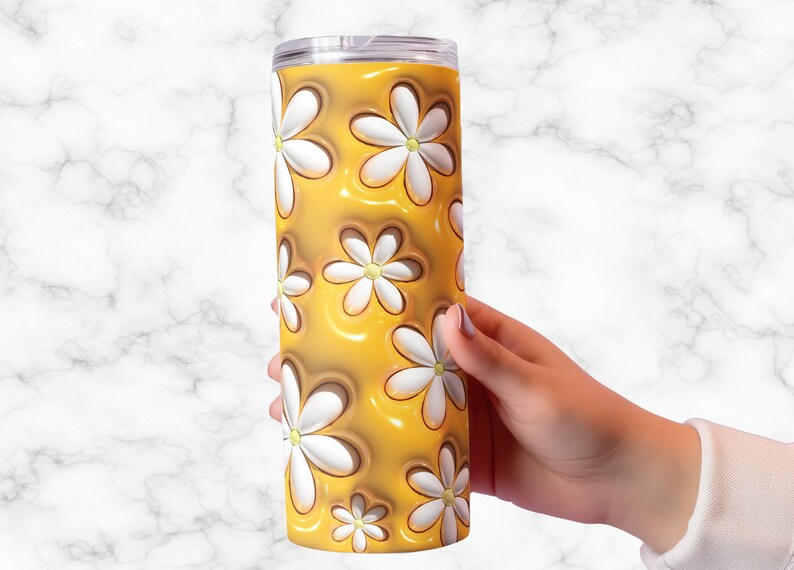 May include: A tall, cylindrical tumbler with a clear lid. The tumbler features a repeating pattern of white daisies with yellow centers against a glossy, golden-yellow background. The tumbler is held by a person's hand.