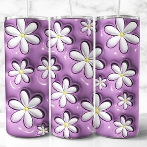 May include: A set of three stainless steel tumblers with a floral design. The design features white daisies with yellow centers against a glossy, lavender background. The tumblers have a straw.