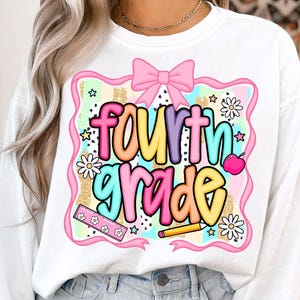 May include: White sweatshirt with a colorful "fourth grade" graphic. The design includes a pink bow, daisies, stars, a ruler, a pencil, and an apple. The text is in a variety of bright colors, perfect for back-to-school.