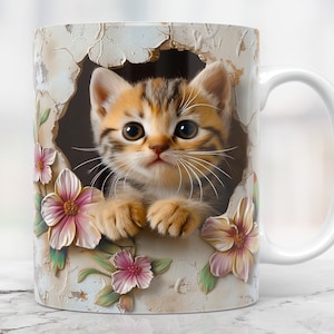 Può includere: Tazza in ceramica bianca con un'immagine colorata di un gattino che spunta da un buco con fiori rosa.