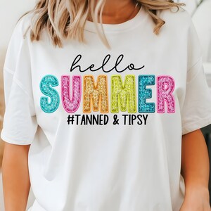 Puede incluir: Camiseta blanca con un gráfico colorido de "hello summer" y el texto "#Tanned & Tipsy" debajo.