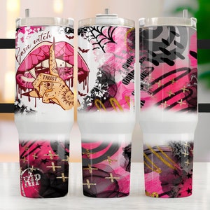 May include: A set of three stainless steel tumblers with a black handle. The tumblers feature a pink and black abstract design with gold accents. One tumbler has a pink mouth with a finger over it and the text "Basic Witch" and "Trust" on it.