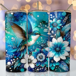 May include: Three stainless steel tumblers with a blue hummingbird and floral design. The hummingbird is flying over blue and white flowers with green leaves. The background is a blue and white watercolor effect.