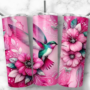 Pode incluir: Um copo rosa com um design vibrante de beija-flor. O copo apresenta um estilo aquarela com flores rosa, folhas e borboletas. O beija-flor tem penas coloridas. Inclui um canudo prateado.