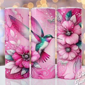 Pode incluir: Um copo rosa com um desenho de um beija-flor com penas rosa, turquesa e roxas, junto a grandes flores rosas e detalhes de glitter prateado. O design inclui elementos florais e de folhas, com o texto "Josie Tumbler".