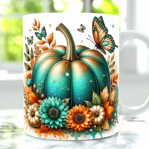 Puede incluir: Una taza de cerámica blanca con un diseño de calabaza azul verdosa y dorada. La calabaza está rodeada de hojas de otoño, flores y mariposas.