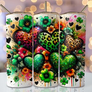 May include: Three stainless steel tumblers with a white background and a colorful design of hearts, flowers, and shamrocks. The hearts are covered in glitter and have leopard print patterns.