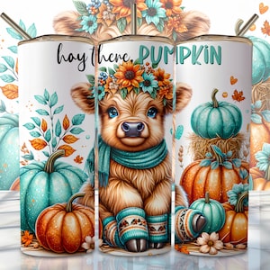 May include: A white tumbler with a brown and white highland cow wearing a blue scarf and a flower crown. The tumbler has the text "hay there, PUMPKIN" on it. The background is a fall theme with pumpkins, leaves, and flowers.