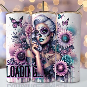 May include: A white stainless steel tumbler with a colorful design featuring a woman with a sugar skull makeup, flowers, and butterflies. The text "Sarcasm Loading..." is printed on the tumbler.