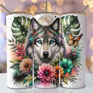 May include: A white tumbler with a colorful design featuring a wolf's face surrounded by flowers and a butterfly. The wolf has blue eyes and a gray and white coat.