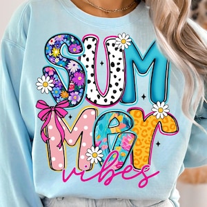 May include: Light blue sweatshirt with the words "SUMMER vibes" in colorful, decorative letters. The "S" is filled with flowers, the "U" has black polka dots, and the "M" is pink with white polka dots. Daisies and a pink bow accent the design.