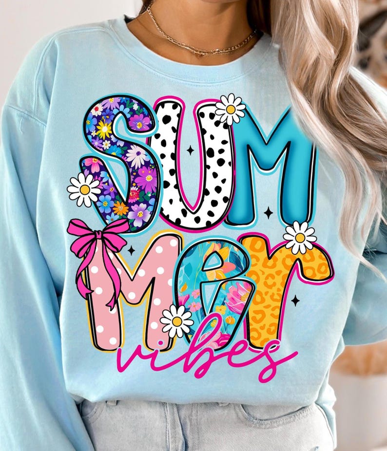 May include: Light blue sweatshirt with the words "SUMMER vibes" in colorful, decorative letters. The "S" is filled with flowers, the "U" has black polka dots, and the "M" is pink with white polka dots. Daisies and a pink bow accent the design.