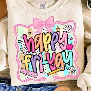 May include: Cream-colored sweatshirt with a colorful graphic that says "Happy Fri-Yay." The design includes a pink bow, stars, flowers, a ruler, a pencil, and a pink apple. The text is in various bright colors.