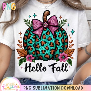 May include: White t-shirt featuring a teal leopard print pumpkin with a pink bow, surrounded by fall foliage and the words "Hello Fall." The design includes orange, pink, and teal accents, perfect for autumn.