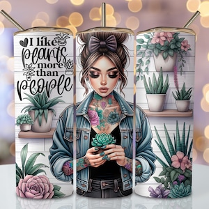 Puede incluir: Un vaso de acero inoxidable con fondo blanco y un diseño de una mujer con un tatuaje floral sosteniendo una planta en maceta. El texto "Me gustan más las plantas que las personas" está en el lado izquierdo del vaso.