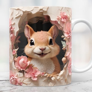 May include: A white ceramic mug with a handle features a smiling squirrel peeking out of a hole decorated with pink flowers. The squirrel is brown and has a white belly.