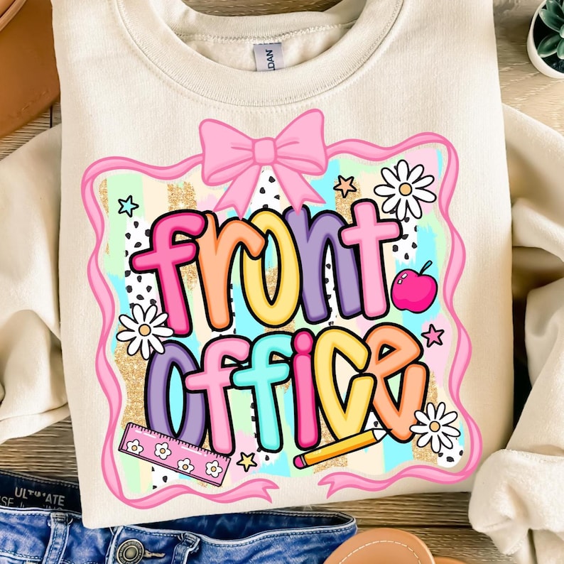 Może przedstawiać: Kremowa bluza z kolorową grafiką "Front Office". Projekt zawiera r&oacute;żową kokardę, stokrotki, gwiazdki, linijkę, oł&oacute;wek i jabłko. Tekst jest w r&oacute;żnych kolorach, obrysowany na czarno.
