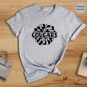 May include: Gray athletic heather t-shirt with a black and white pom-pom design and the word "COUGARS" in a black banner.