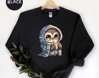 May include: Black sweatshirt with a cute cartoon owl wearing a blue scarf and holding a cup of hot cocoa. The owl is wearing a blue and white scarf and has big brown eyes.