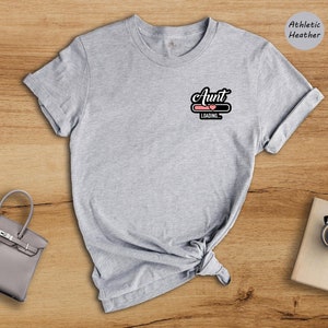 May include: Gray t-shirt with the text "Aunt Loading..." in black with a pink heart graphic. The shirt is made of athletic heather fabric.