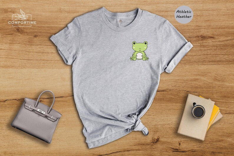 Op de afbeelding: Grijs T-shirt met een groene kikker afbeelding op de voorkant. Het shirt is gemaakt van athletic heather stof.