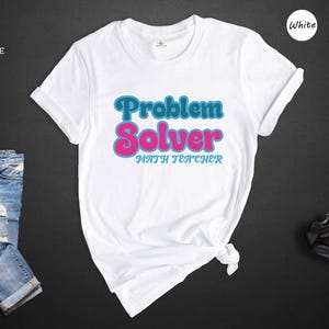 May include: White t-shirt with the text "Problem Solver Math Teacher" in blue and pink retro font.