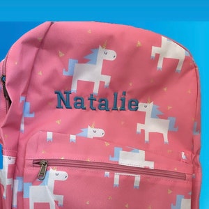 May include: Pink unicorn backpack with a zippered pocket and the name "Natalie" embroidered on the front. The backpack has a white label with the text "Basic Packs by Little Fox Original Design Est. 2016".