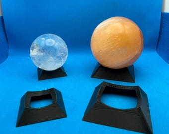Puede incluir: Cuatro soportes de exhibición cuadrados de color negro, impresos en 3D, para bolas de cristal. Dos soportes sostienen una bola de cristal transparente y una bola de cristal naranja claro.