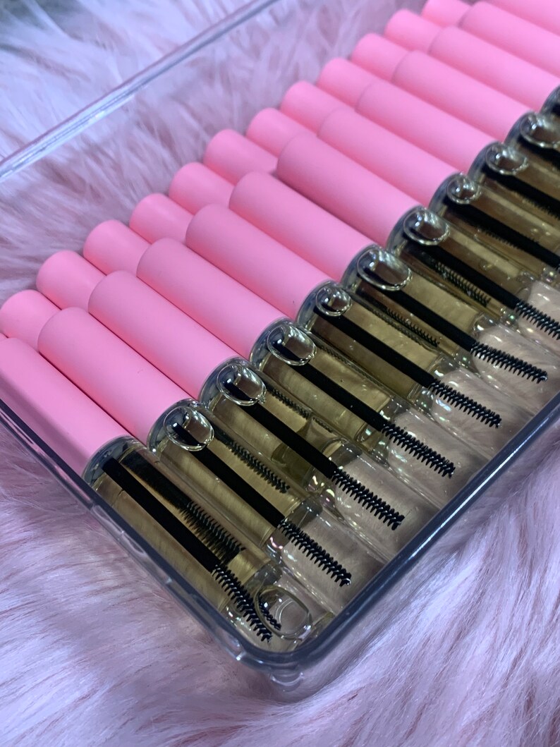 K&ouml;nnte beinhalten: Ein transparenter Plastikbeh&auml;lter gef&uuml;llt mit mehreren rosa und durchsichtigen R&ouml;hrchen, die eine klare Fl&uuml;ssigkeit mit einem schwarzen Applikatorpinsel enthalten. Die R&ouml;hrchen sind in Reihen angeordnet.
