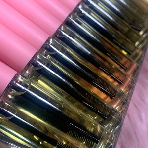K&ouml;nnte beinhalten: Ein durchsichtiger Plastikbeh&auml;lter mit mehreren Reihen kleiner, durchsichtiger R&ouml;hrchen, die mit einer klaren Fl&uuml;ssigkeit und schwarzen Mascara-Wands gef&uuml;llt sind.