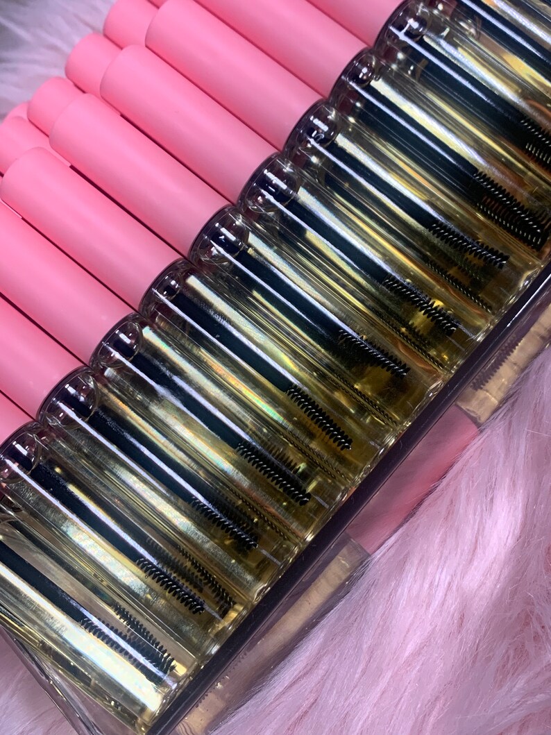 K&ouml;nnte beinhalten: Nahaufnahme einer durchsichtigen Glasflasche mit einem schwarzen Applikatorpinsel. Die Flasche ist mit einer klaren Fl&uuml;ssigkeit gef&uuml;llt und hat einen rosa Deckel. Die Flaschen sind in einer Reihe auf einer rosa Oberfl&auml;che angeordnet.