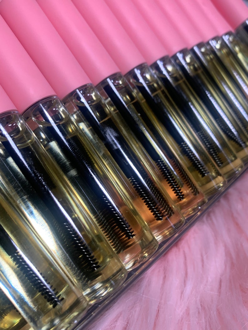 K&ouml;nnte beinhalten: Nahaufnahme von mehreren durchsichtigen Glasflaschen mit schwarzen Applikatorst&auml;bchen. Die Flaschen sind mit einer hellgelben Fl&uuml;ssigkeit gef&uuml;llt und in Reihen auf einer rosa Oberfl&auml;che angeordnet.