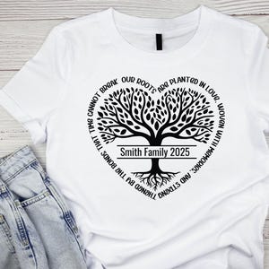 May include: White t-shirt with a black tree design and the text "TIME CANNOT BREAK OUR ROOTS ARE PLANTED IN LOVE, WOVEN WITH MEMORIES, AND STRENGTHENED BY THE BONDS THAT TIME CANNOT BREAK" around the tree. The tree has a banner that says "Smith Family 2025".