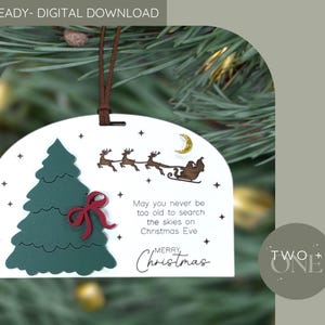 May include: A white Christmas ornament with a green Christmas tree, red bow, and a sleigh with reindeer. The ornament has the text "May you never be too old to search the skies on Christmas Eve. Merry Christmas."