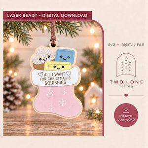 Peut inclure: Une décoration de Noël en bois en forme de chaussette, avec une base rose clair ornée de flocons de neige blancs. La chaussette contient trois personnages squishy dessinés et une bannière blanche avec le texte ALL I WANT FOR CHRISTMAS IS SQUISHIES.