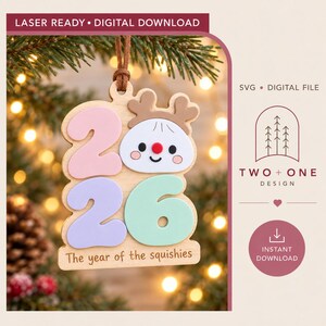 Può includere: Un file di download digitale pronto per il laser per un ornamento in legno con l'anno 2026 in rosa e viola pastello, un volto di renna cartoon e il testo The year of the squishies, SVG digital file e la scritta Two + One Design.
