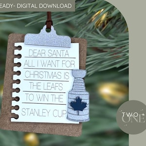 Könnte beinhalten: Weihnachtsschmuck in Notizblockform mit dem Text „LIEBER WEIHNACHTSMANN, ALLES, WAS ICH ZU WEIHNACHTEN MÖCHTE, IST, DASS DIE LEAFS DEN STANLEY CUP GEWINNEN.“ Enthält einen silberfarbenen Stanley Cup und ein blaues Ahornblatt.