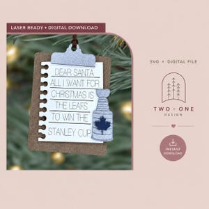 May include: A clipboard-shaped ornament featuring a white paper insert with the text: DEAR SANTA ALL I WANT FOR CHRISTMAS IS THE LEAFS TO WIN THE STANLEY CUP. A silver glitter hockey trophy with a dark blue maple leaf sits on the right side.