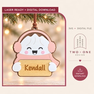 Puede incluir: Un adorno de madera con un personaje de bola de masa blanco con cara sonriente, que lleva orejeras y bufanda rosas. El personaje sostiene un letrero de madera clara con el nombre Kendall grabado. El texto incluye LASER READY, DIGITAL DOWNLOAD, SVG, DIGITAL FILE, TWO + ONE DESIGN e INSTANT DOWNLOAD.