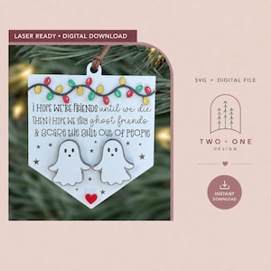 May include: A white, shield-shaped wooden ornament featuring two white ghost figures, a red heart, and a string of colorful Christmas lights. The text reads: I HOPE WE'RE FRIENDS until we die THEN I HOPE WE STAY ghost friends & SCARE THE SHIT OUT OF PEOPLE.