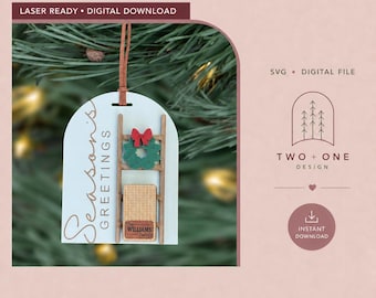May include: An arched ornament featuring the text Season's Greetings, a wooden ladder, a green wreath with a red bow, and a small rectangular sign labeled The Williams Family. The design is a laser-ready digital file for crafting holiday decor.