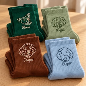 Puede incluir: Cuatro pares de calcetines acanalados en verde oscuro, verde salvia, marrón y azul claro. Cada par presenta una cara de perro bordada y un nombre: Momo en el verde oscuro, Nugget en el verde salvia y Cooper en los calcetines marrones y azules.