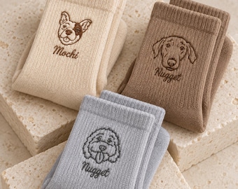May include: Three pairs of ribbed socks in cream, brown, and light grey. Each pair features an embroidered dog face and a name: Mochi on the cream pair, Nugget on the brown pair, and Nugget on the light grey pair.