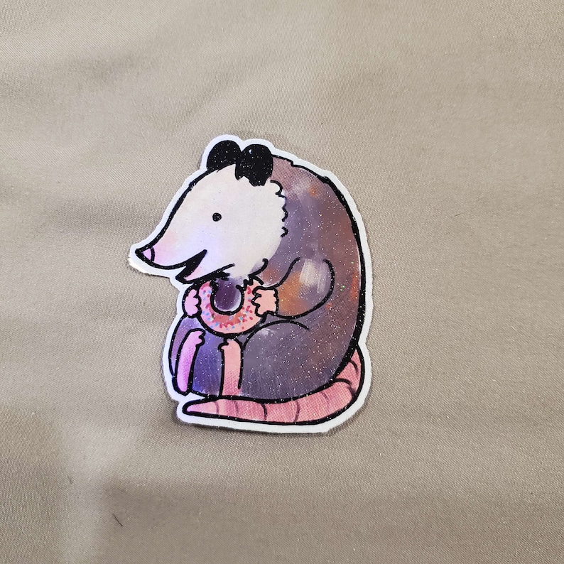 May include: A cartoon illustration of a possum holding a pink and white doughnut. The possum is grey with a white face and black eyes. The doughnut has pink icing and white sprinkles.