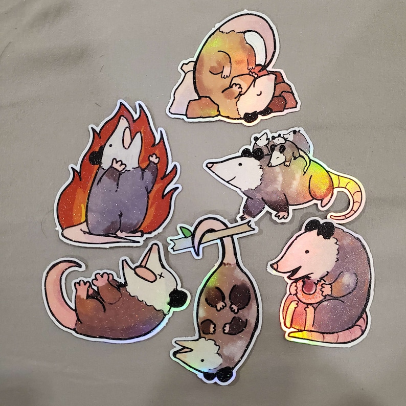 May include: Set of nine iridescent vinyl stickers featuring various opossums in different poses. The stickers are holographic and have a rainbow sheen. Some of the opossums are holding sticks, while others are carrying babies on their backs. One opossum is surrounded by flames.